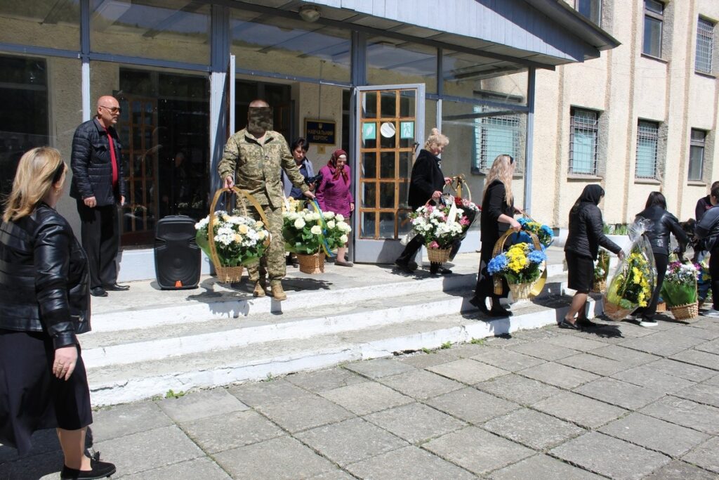 Люди з квітами виходять із будівлі.