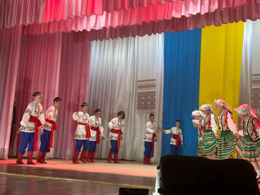 Діти танцюють в українських народних костюмах на сцені.