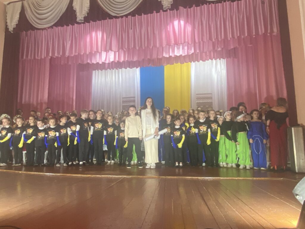 Діти на сцені в костюмах перед завісою.