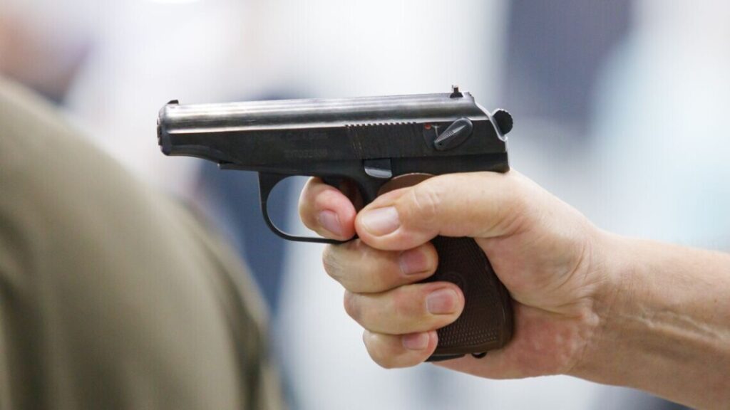 Рука тримає пістолет на білому фоні.