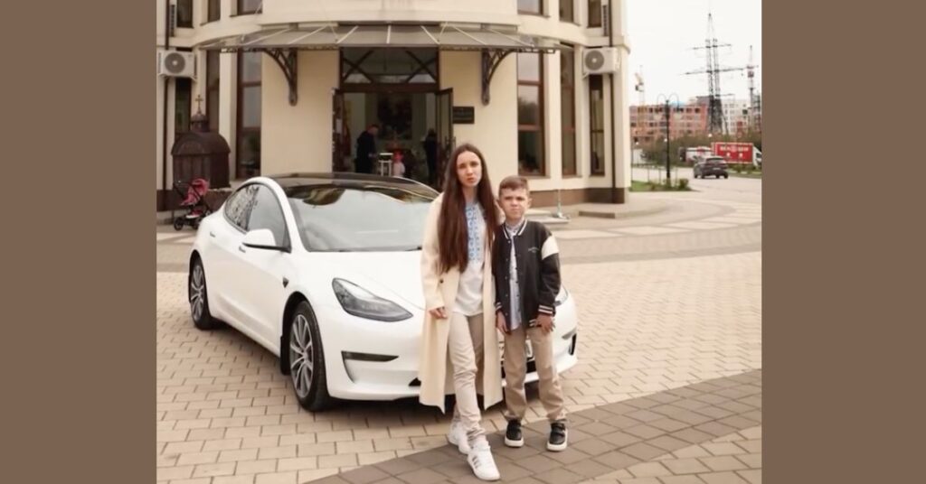Жінка з дитиною біля білої Tesla біля будівлі.