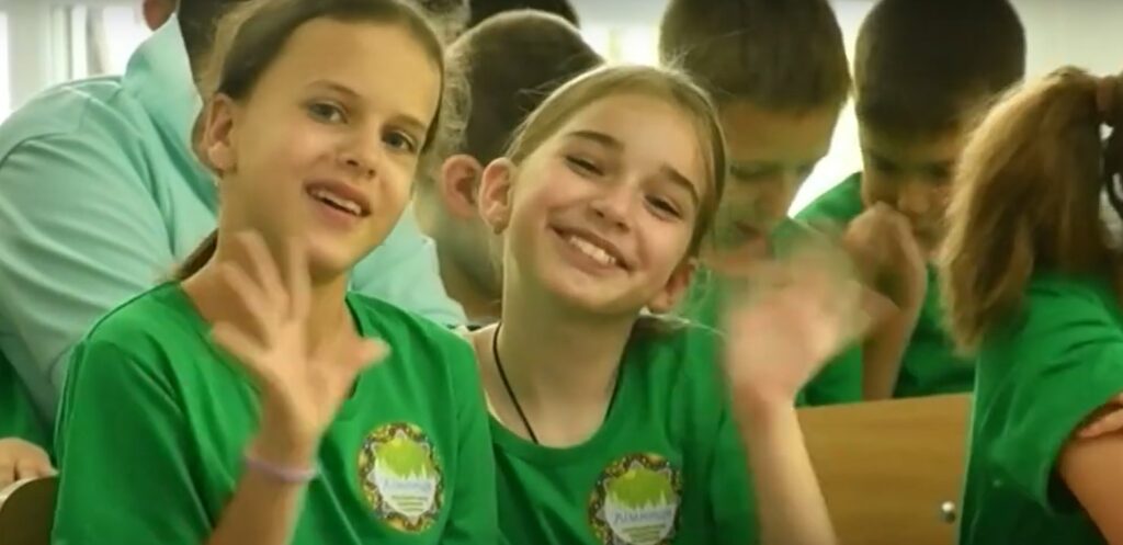 Діти в зелених футболках махають руками