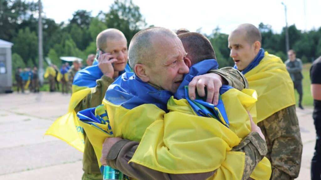 Військові обіймаються, накриті українськими прапорами.