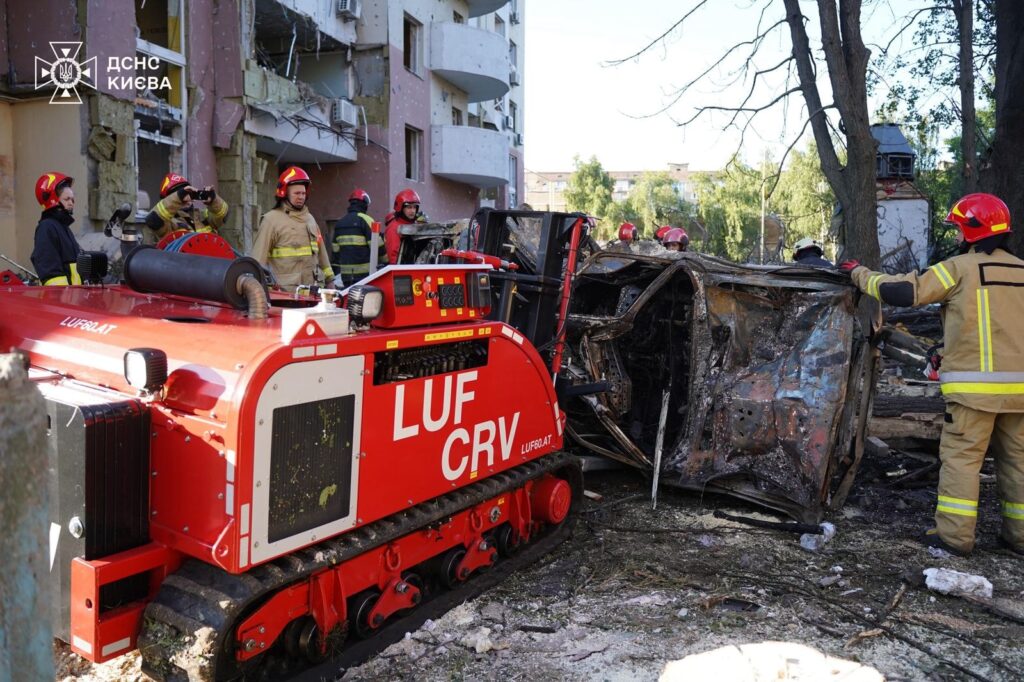 Пожежники оглядають зруйнований автомобіль у Києві.