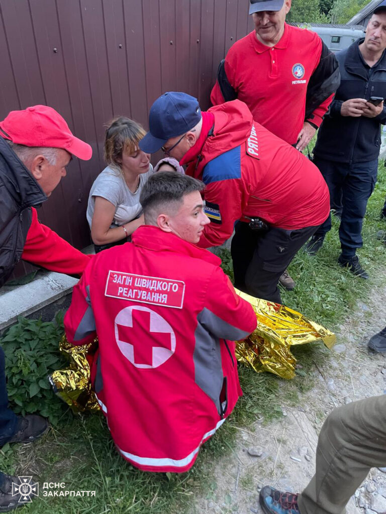 Рятувальники допомагають жінці біля стіни на вулиці.