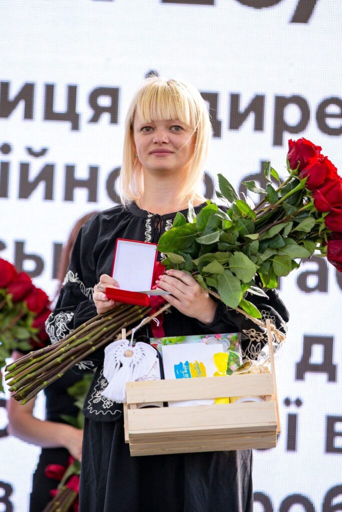 Жінка з квітами та грамотою на сцені