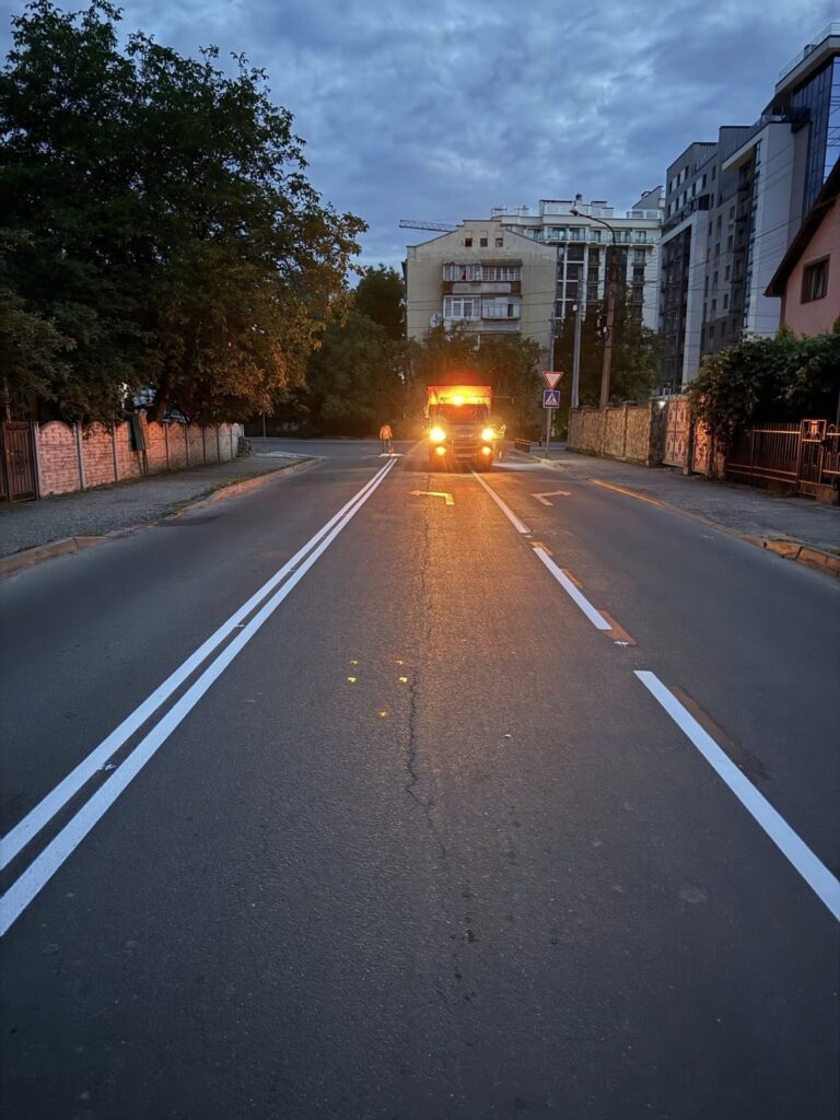 Вантажівка з увімкненими фарами на вулиці ввечері.