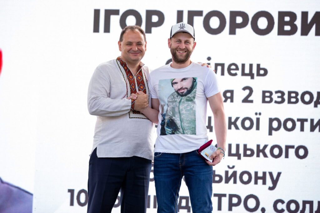 Двоє чоловіків потискають руки на сцені.