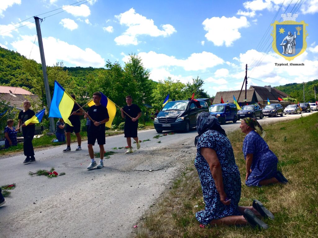Люди з прапорами на вулиці біля автомобілів.