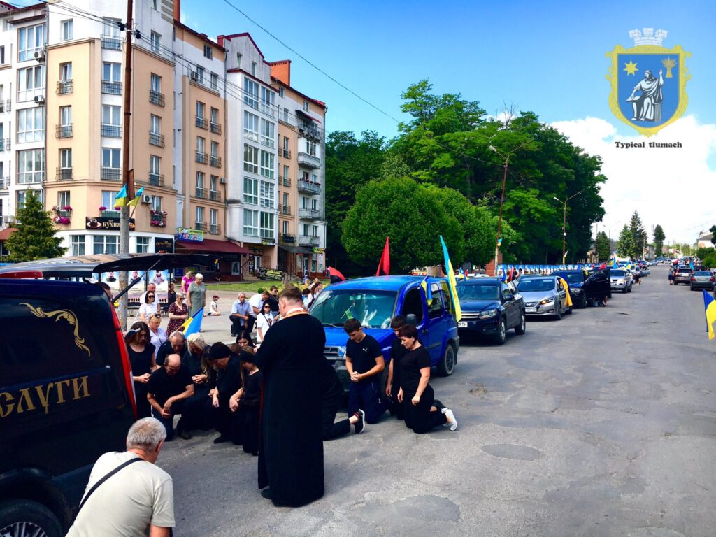 Люди на колінах біля траурного кортежу в місті.