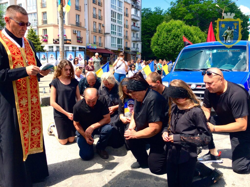 Люди на колінах під час церемонії з прапорами.
