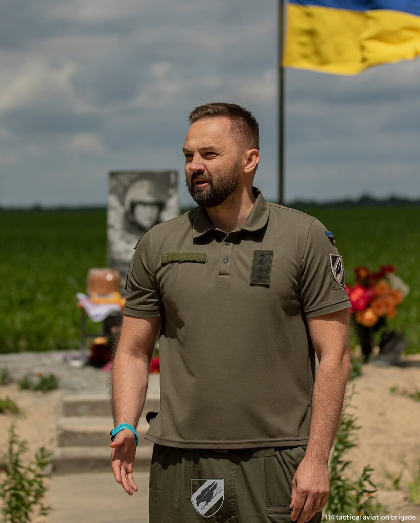 Чоловік у військовій формі перед українським прапором.