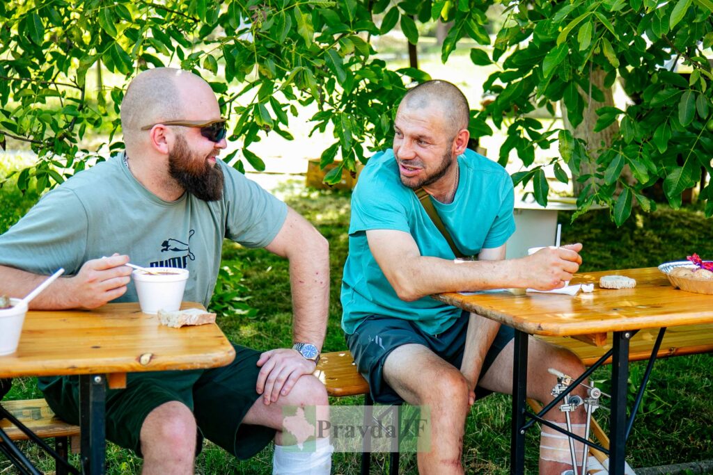 Двоє чоловіків розмовляють за столом на природі.