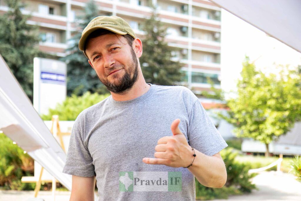 Чоловік з бородою у футболці та кепці на відкритому повітрі.
