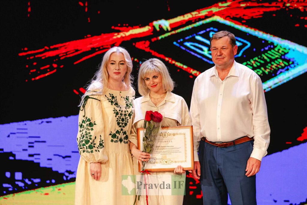 Троє людей з грамотою та трояндами на сцені.