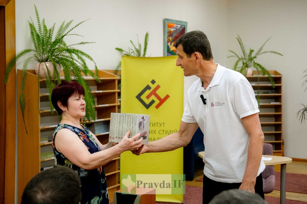 Жінка передає книжки чоловікові у приміщенні бібліотеки.