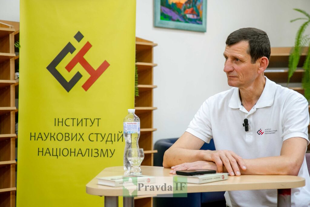 Людина сидить біля банера Інституту наукових студій.