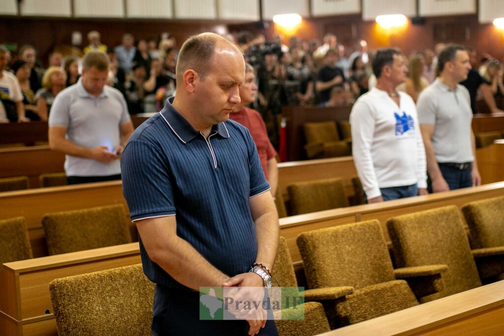 Люди стоять у залі, багато сидячих місць.