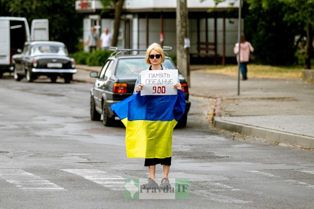 Людина з українським прапором і плакатом на вулиці.