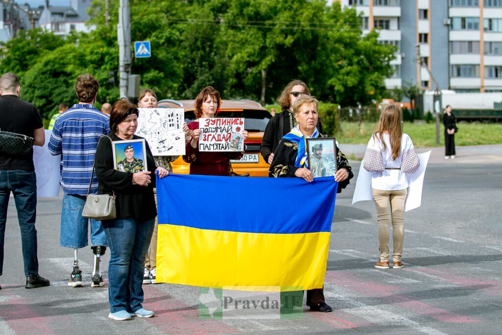 Люди з плакатами та прапором України на демонстрації.