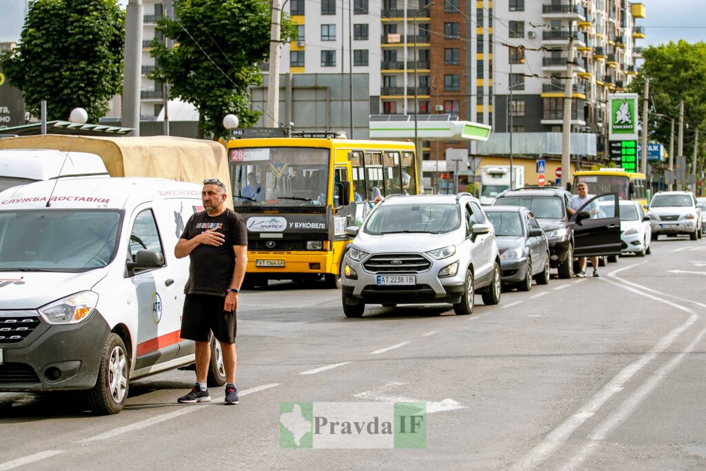 Люди стоять біля автомобілів на міській дорозі.