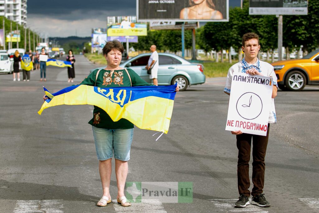 Люди з плакатами та українським прапором на демонстрації.