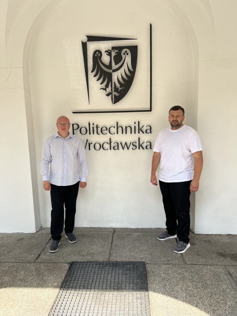 Двоє чоловіків біля логотипу Політехніки Вроцлавської.