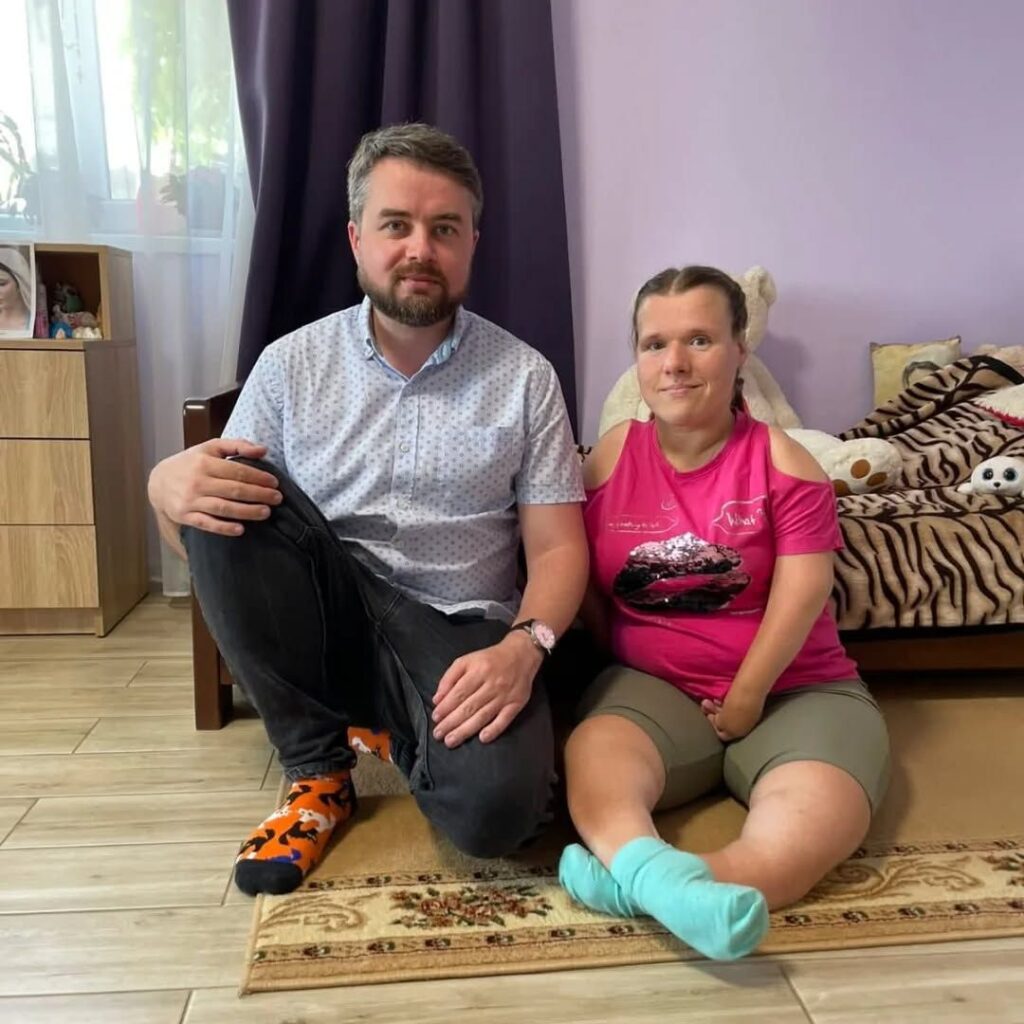 Двоє людей сидять на килимі в кімнаті.