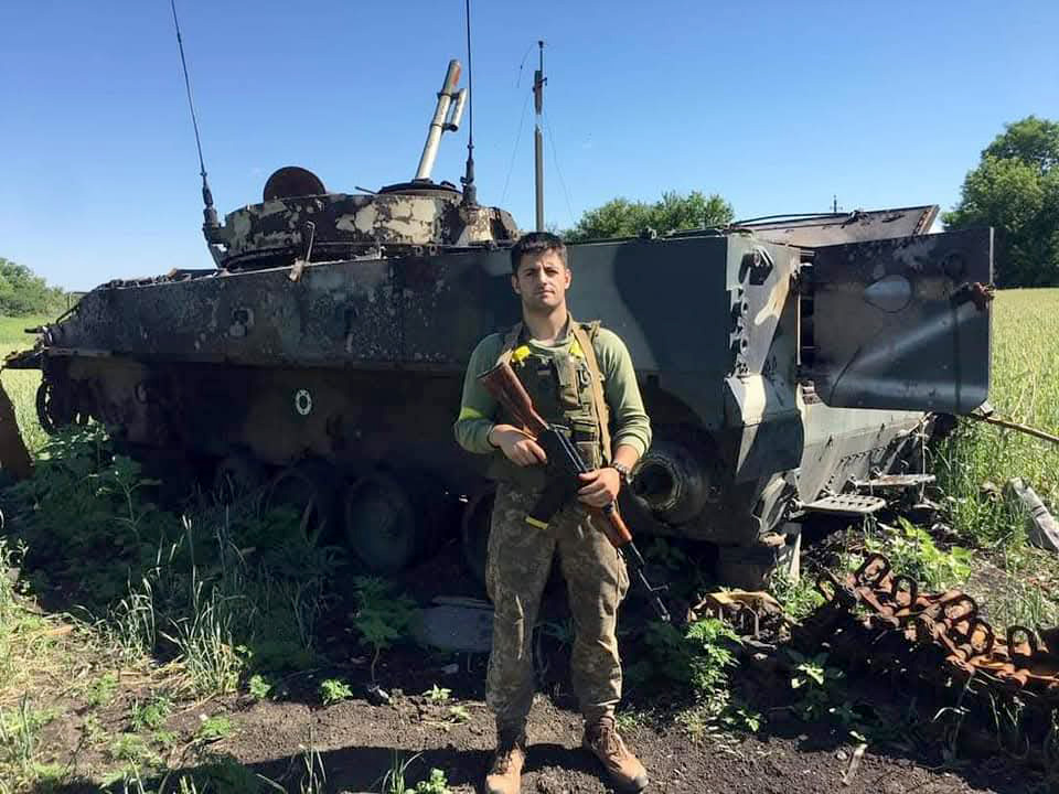 Військовий перед розбитим бронетранспортером на полі бою.