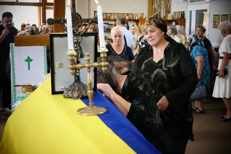 Жінка сумує біля труни з українським прапором