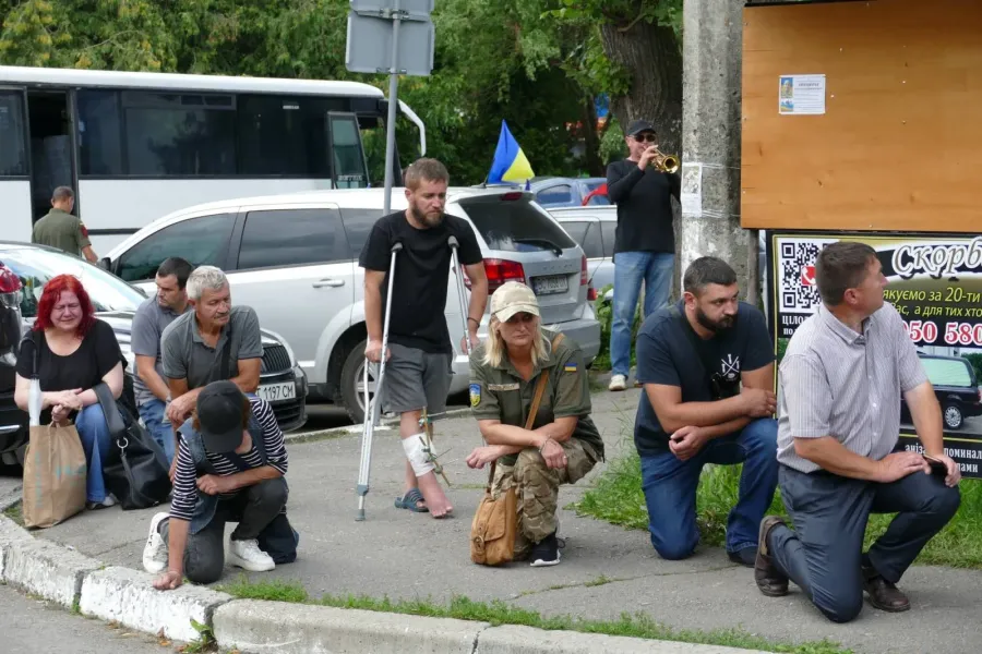 Люди стоять на колінах біля автобусу в Україні.