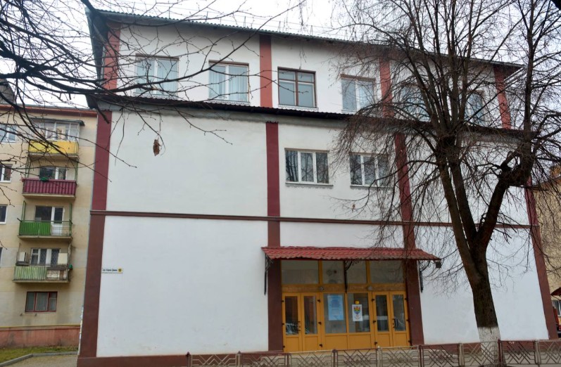 Триповерхова будівля з деревами на фоні.