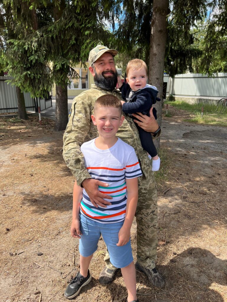 Військовий з дітьми на вулиці під деревами.