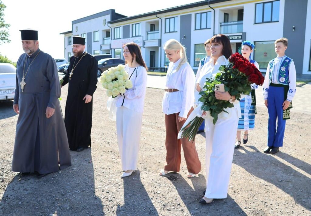 Люди з квітами біля сучасної будівлі.