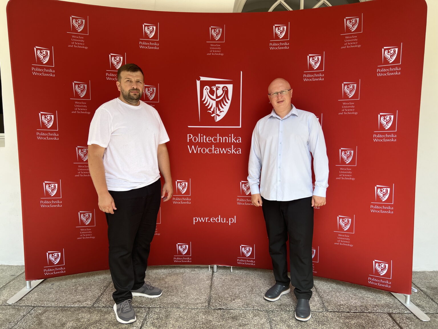 Двоє чоловіків перед логотипом Політехніки Вроцлавської.