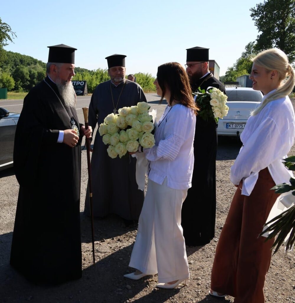 Люди з квітами спілкуються з духовенством на вулиці.