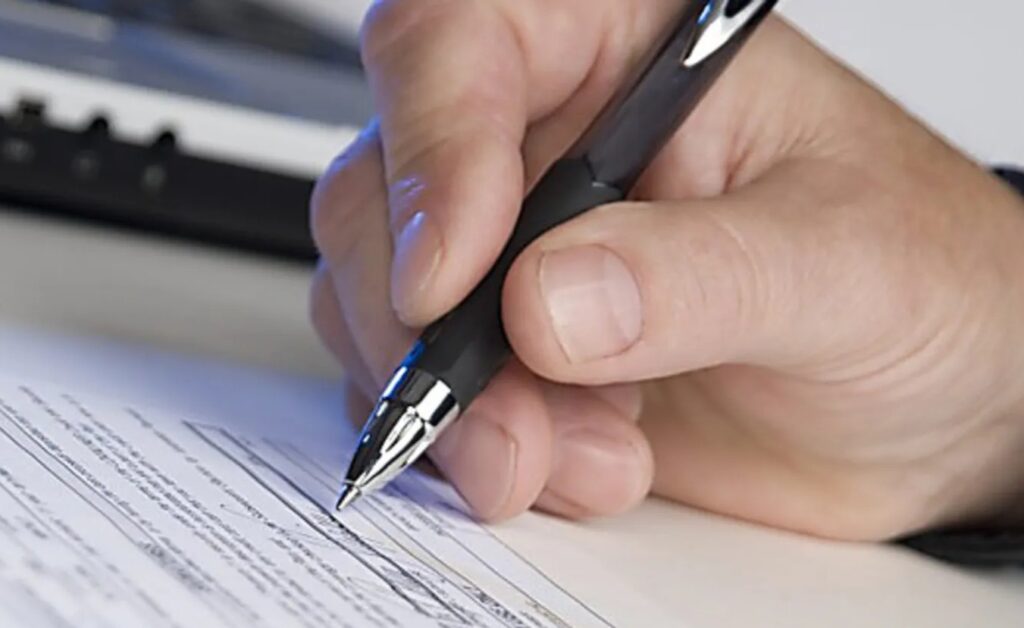Людина підписує документ чорним ручкою