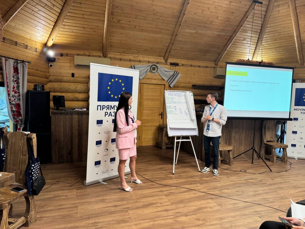 Презентація у дерев'яному залі з проектором та фліпчартом.