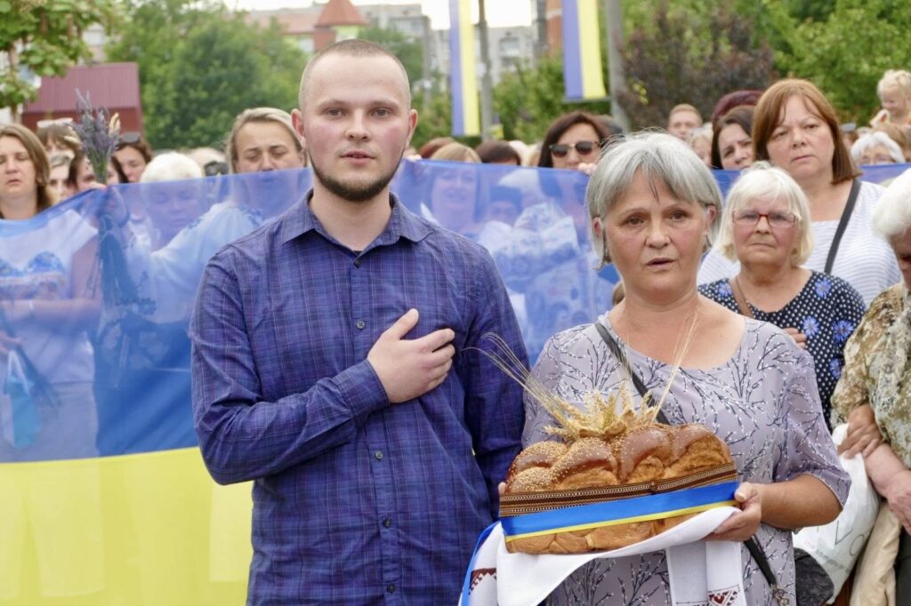 Люди з короваєм на фоні українського прапора.