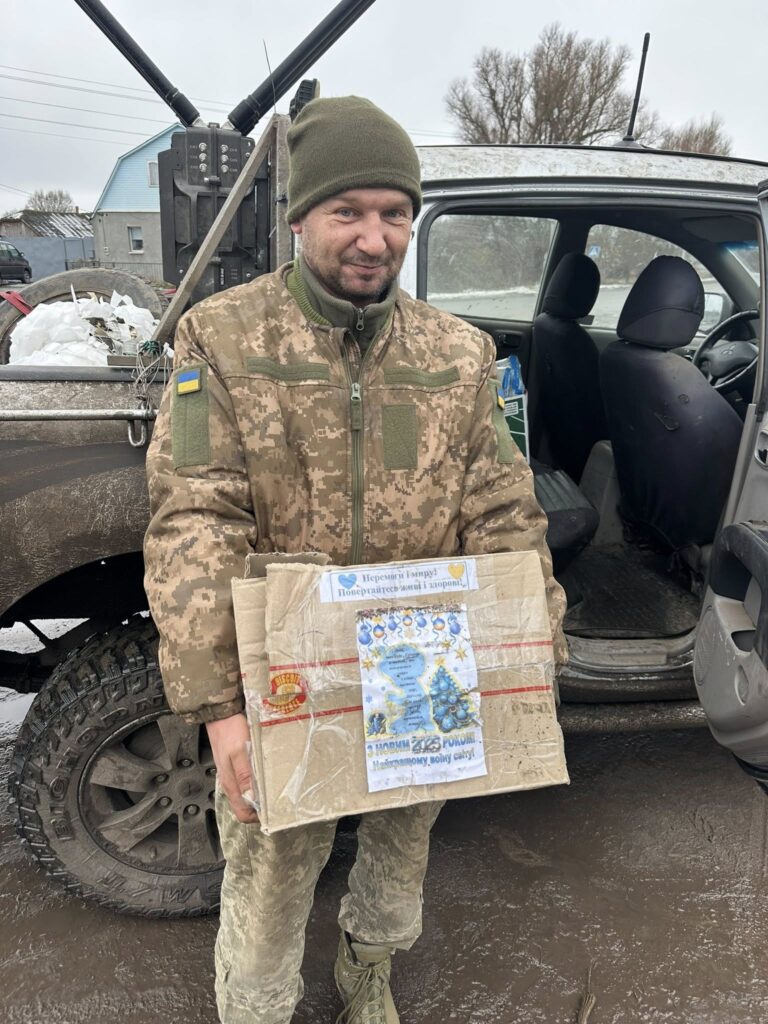 Український військовий з пакунком біля автомобіля.