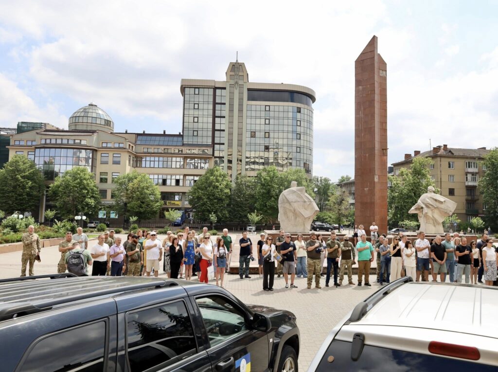 Група людей на площі перед сучасною будівлею.