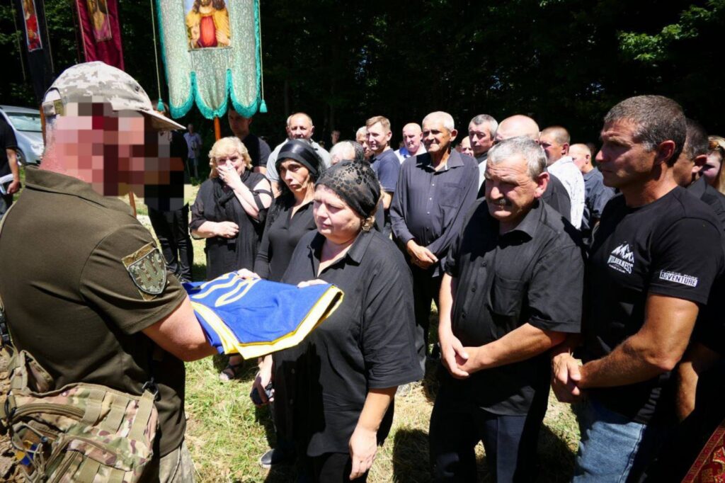 Люди на похороні з українським прапором.