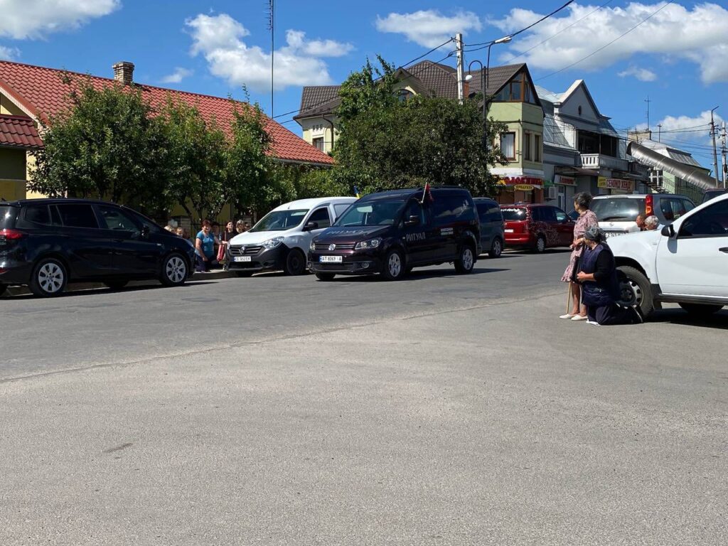 Люди на колінах перед похоронним кортежем на вулиці.