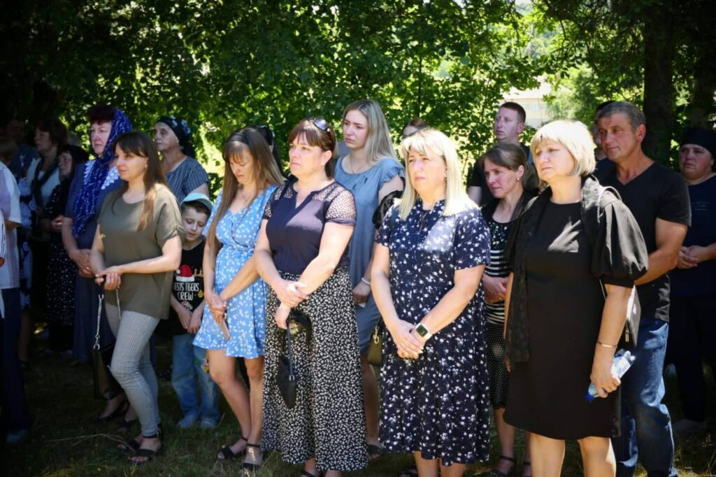 Група людей стоїть під деревами на заході.