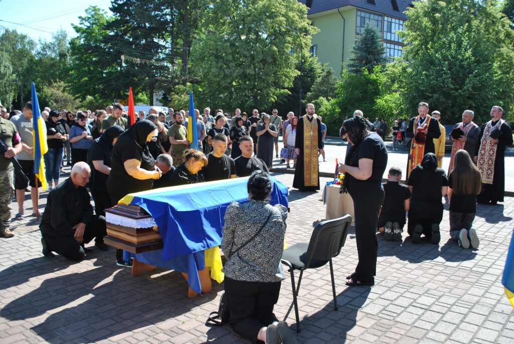 Молитва біля труни з українським прапором на дворі.