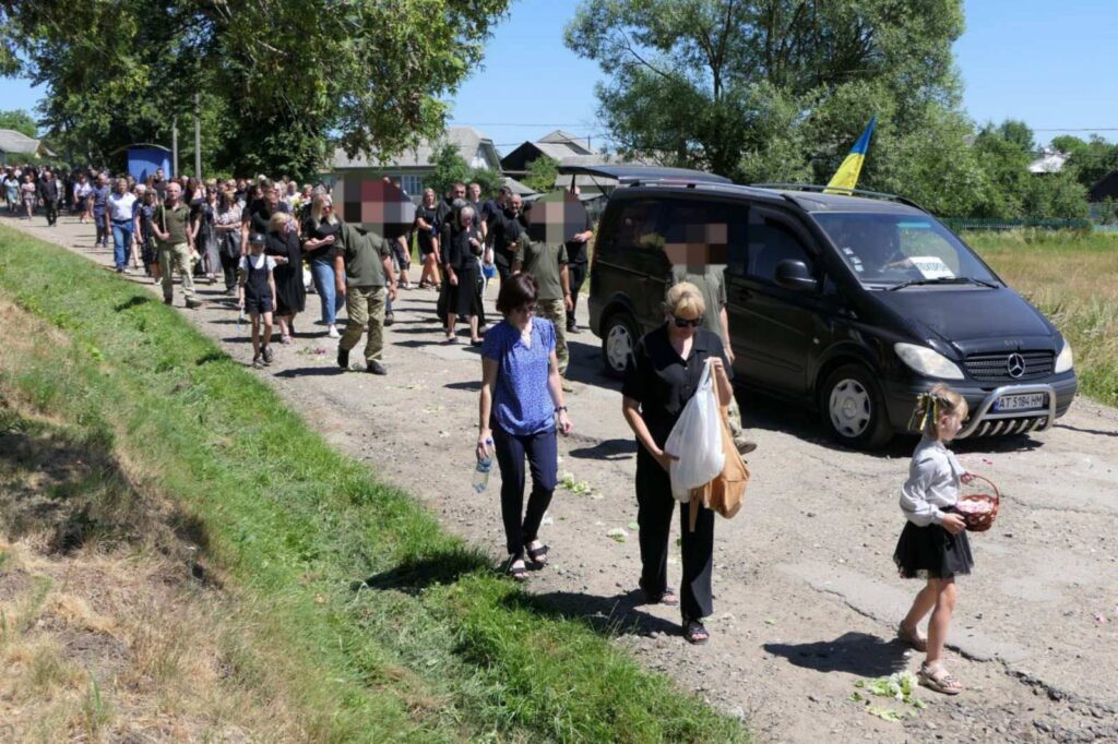 Люди йдуть дорогою, за ними авто з прапором.