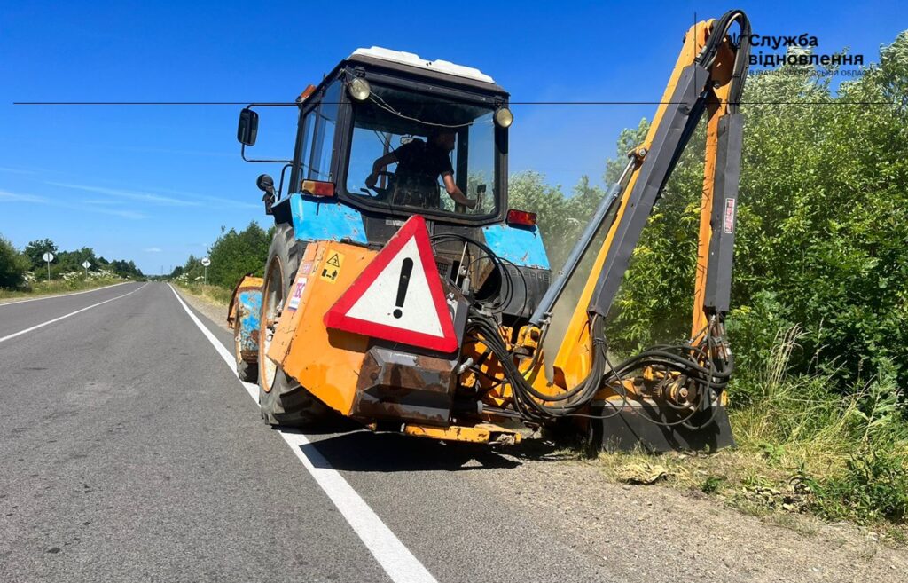 Трактор косить траву біля дороги на природі.