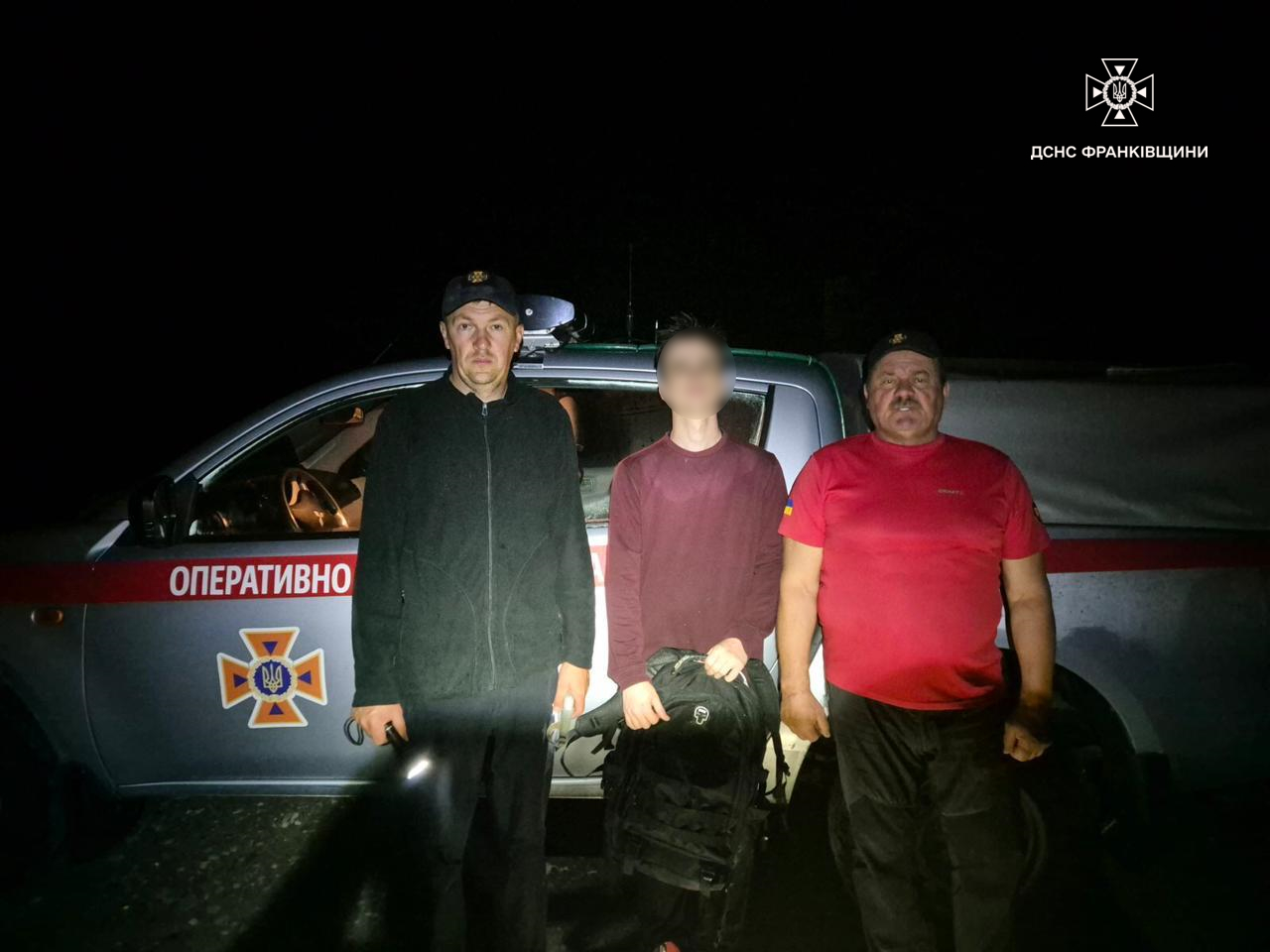 Рятувальники стоять перед службовим автомобілем вночі.