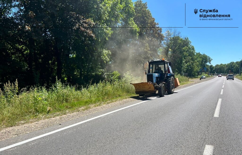 Трактор працює на узбіччі дороги біля лісу.