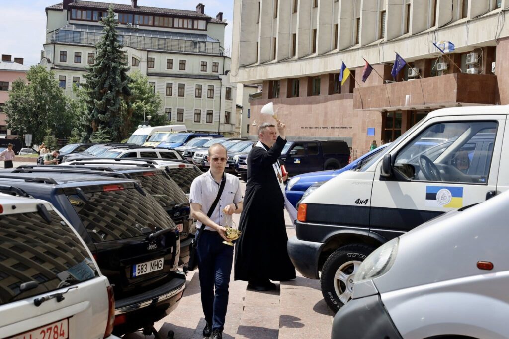 Священник освячує автомобілі перед будівлею в місті
